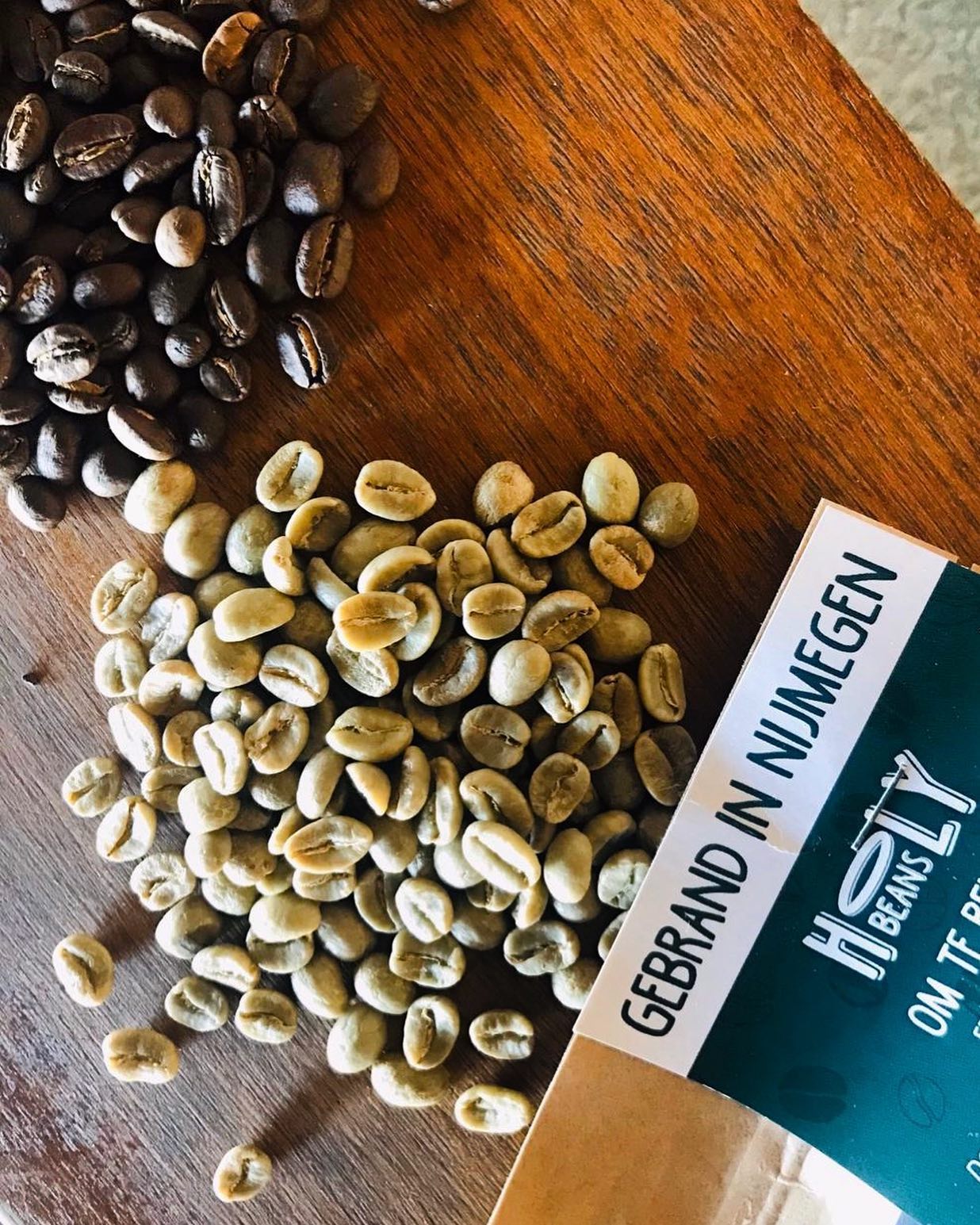 Groene en gebrande koffiebonen naast een zak Holy Beans koffie